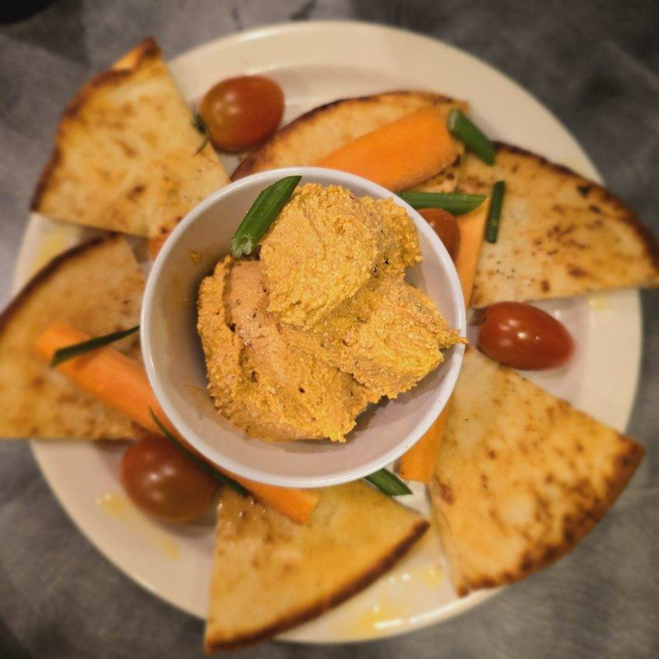 A plate of hummus with pita bread, cherry tomatoes, and carrot sticks at Simo's Pizza.
