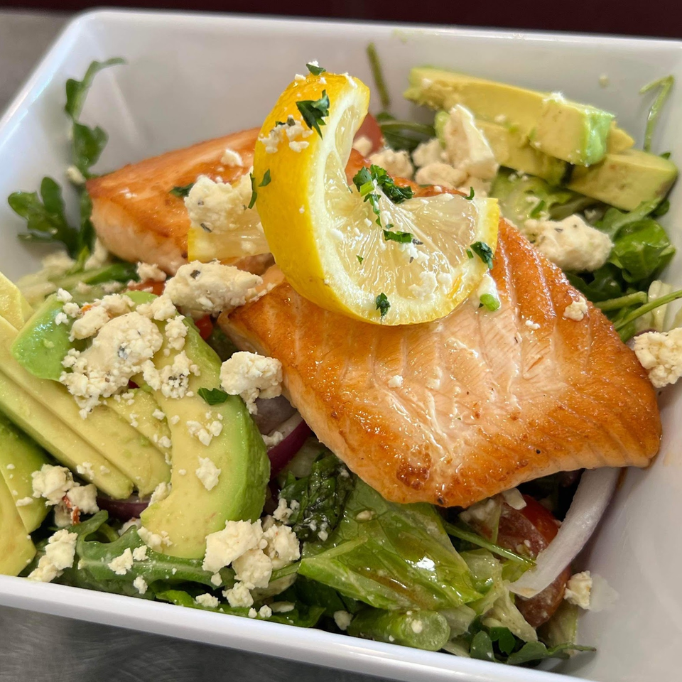 Simo's Pizza salmon salad with avocado, feta cheese, and a lemon wedge in a white bowl.