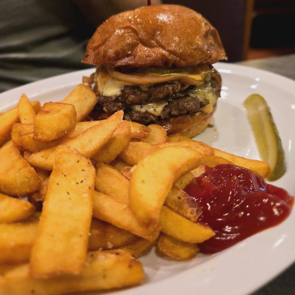 A double cheeseburger with melted cheese, a side of thick-cut fries with ketchup, and a pickle spear.
